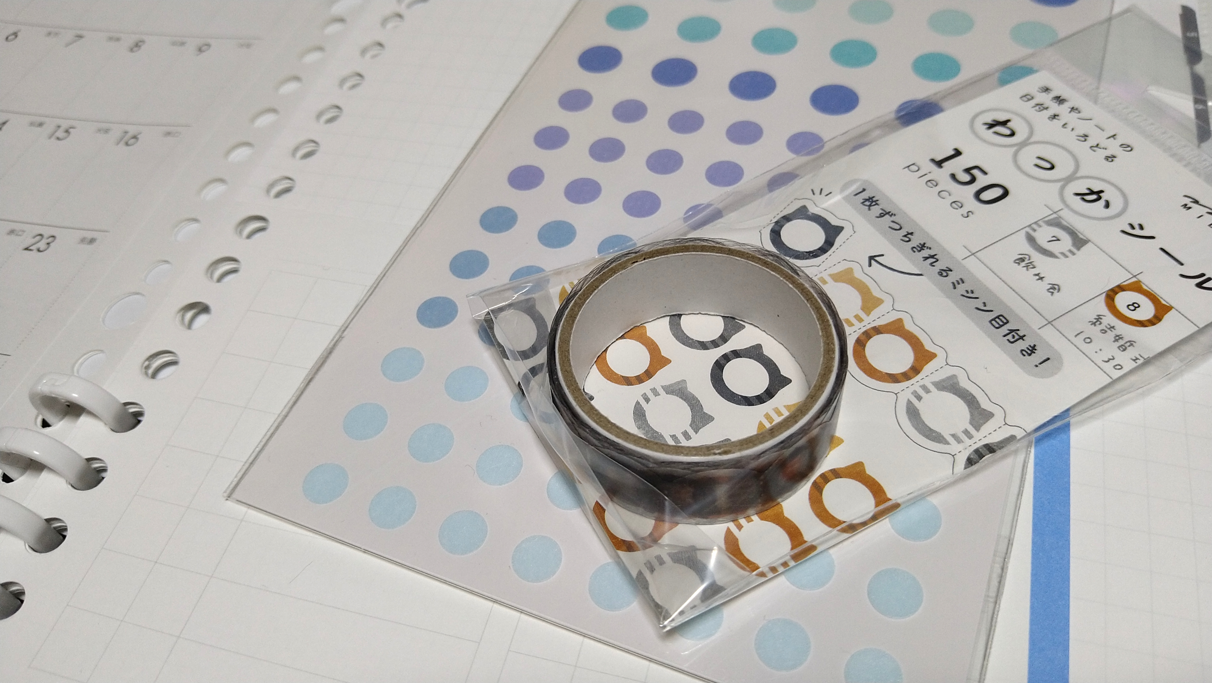 青系グラデーションの丸シールシートの上に猫の顔の形をした「わっかシール」のパッケージと、マスキングテープが置かれている